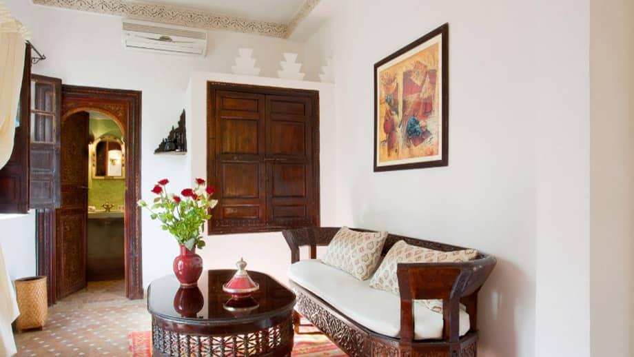 Elegant sofa with cushions beside a dark wooden table and vase in Angsana Riads Collection - Marrakech Blanc Studio King.