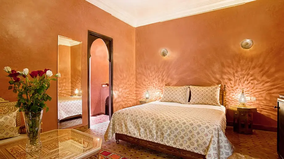 Bed with patterned bedding sits in warmly lit Angsana Riads Collection - Marrakech, Zaouia Deluxe King.