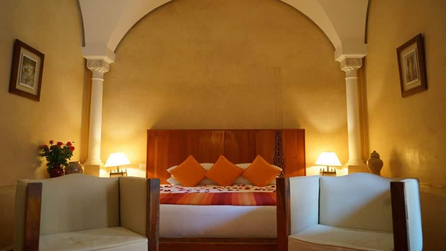 Bed with orange pillows, framed by columns, in cozy Angsana Riads Collection - Marrakech, Lydines Junior Suite.
