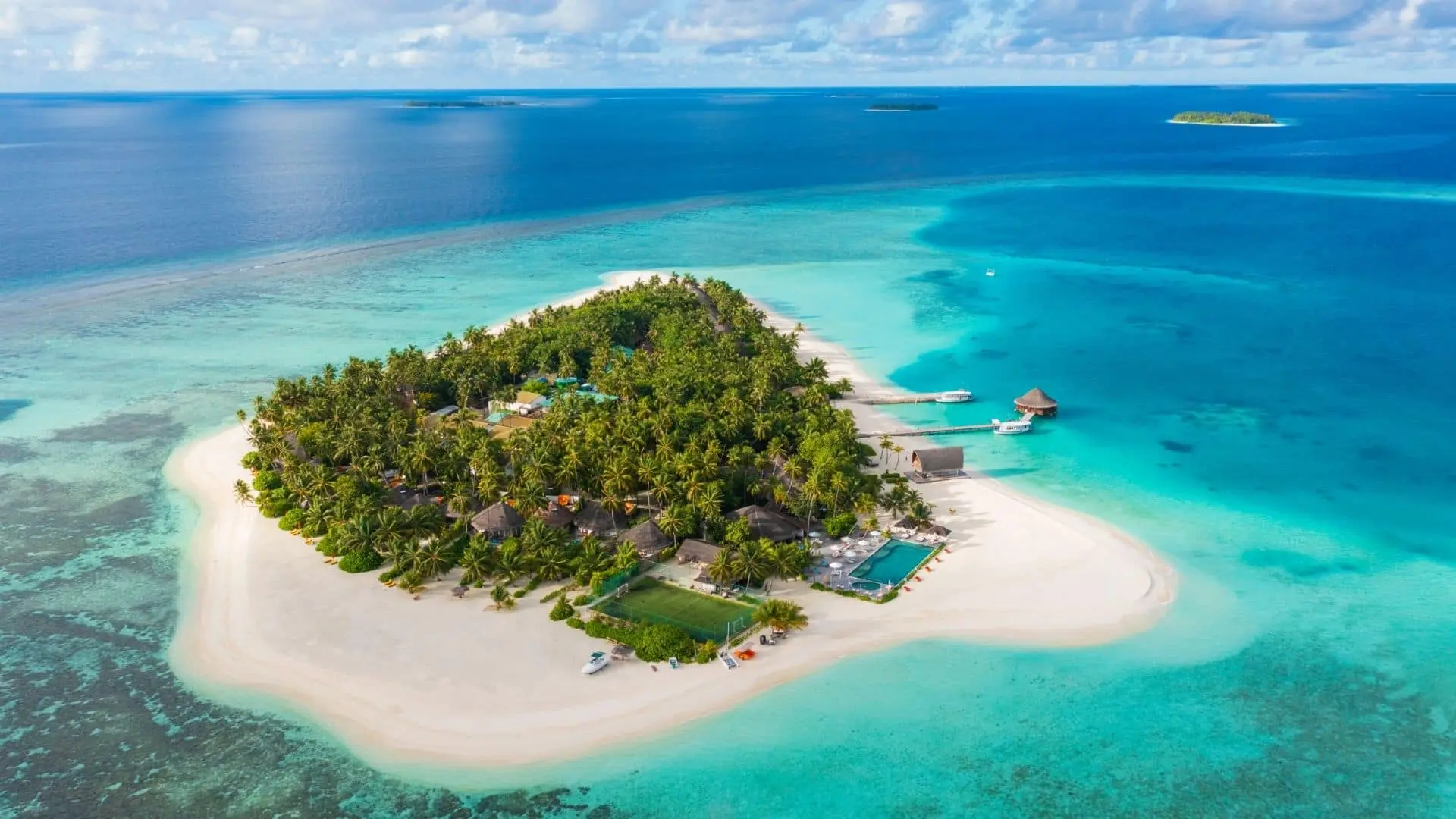 Aerial view of Angsana Velavaru Maldives, an island resort with lush greenery, surrounded by turquoise ocean.