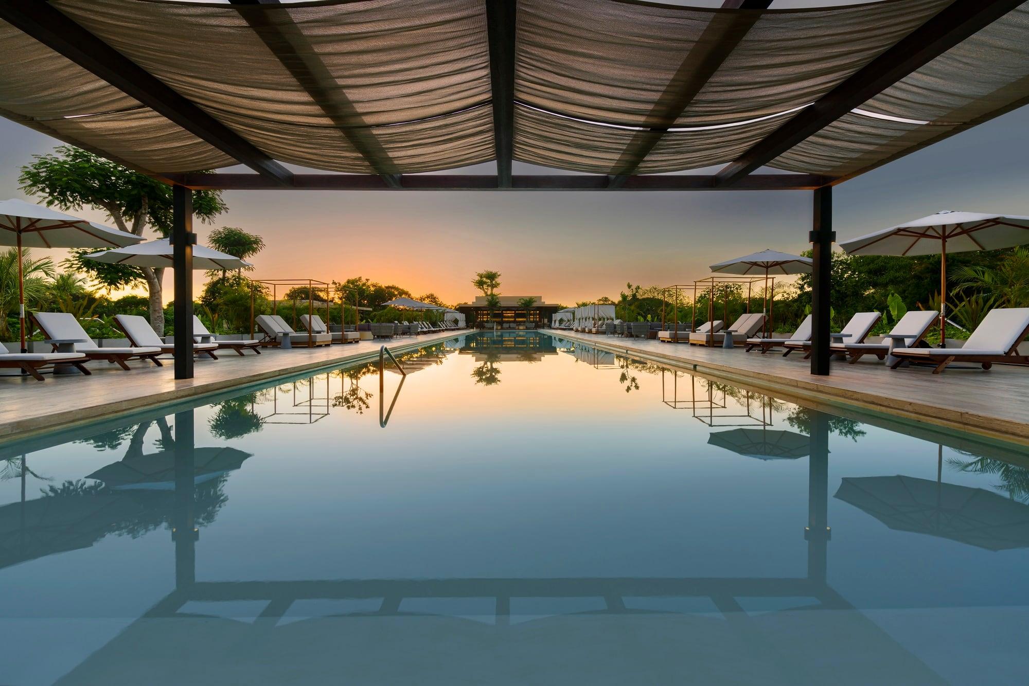 Pool reflecting sunset, surrounded by lounge chairs at Hacienda Xcanatun, Angsana Heritage Collection.