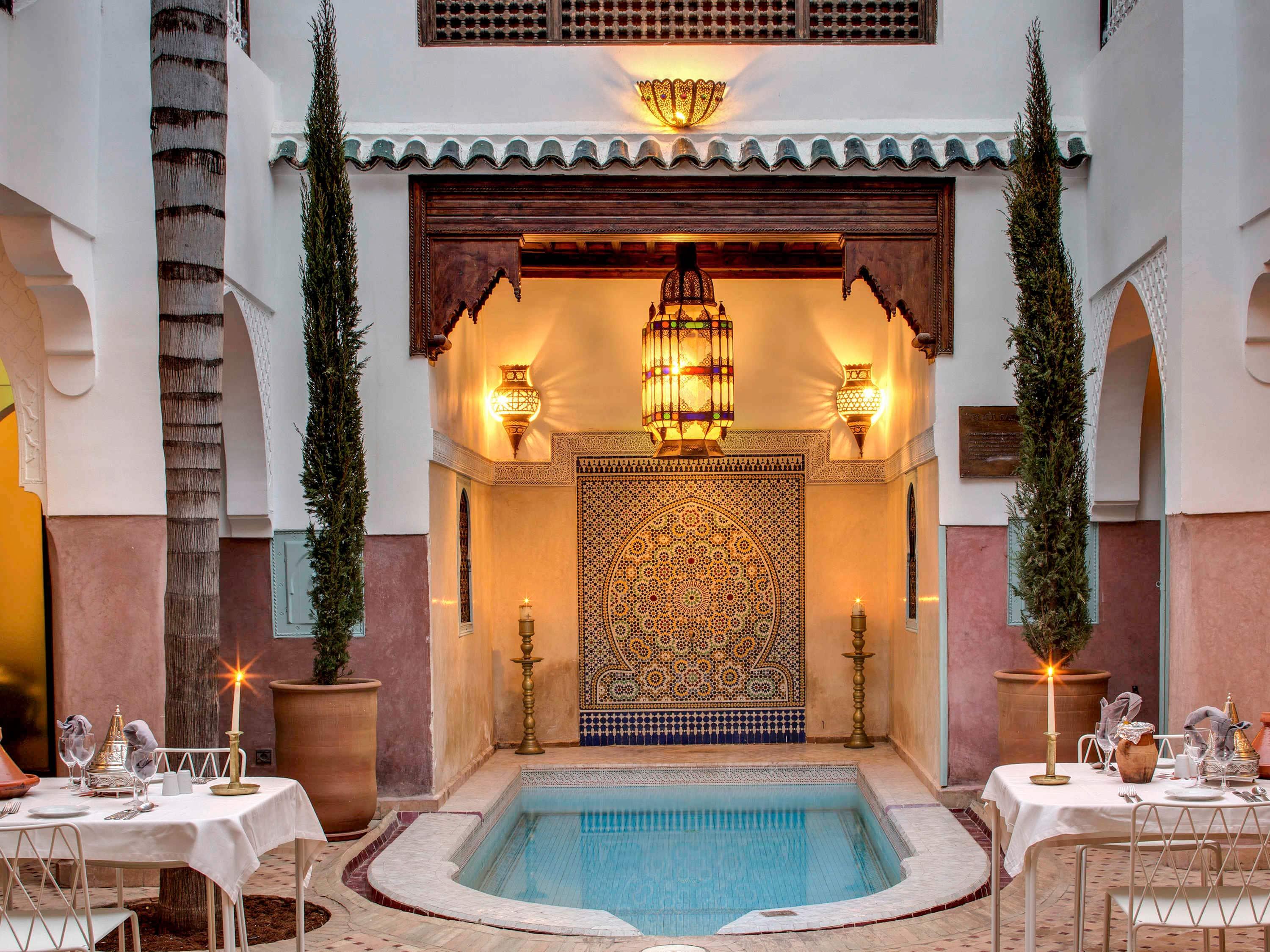Ornate courtyard pool at Angsana Riads Collection, surrounded by decorated tables and glowing lanterns.