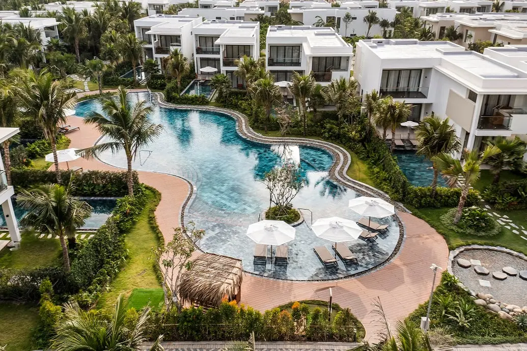 Winding pool amidst villas and palms at Angsana Ho Tram Vietnam, surrounded by lush greenery.