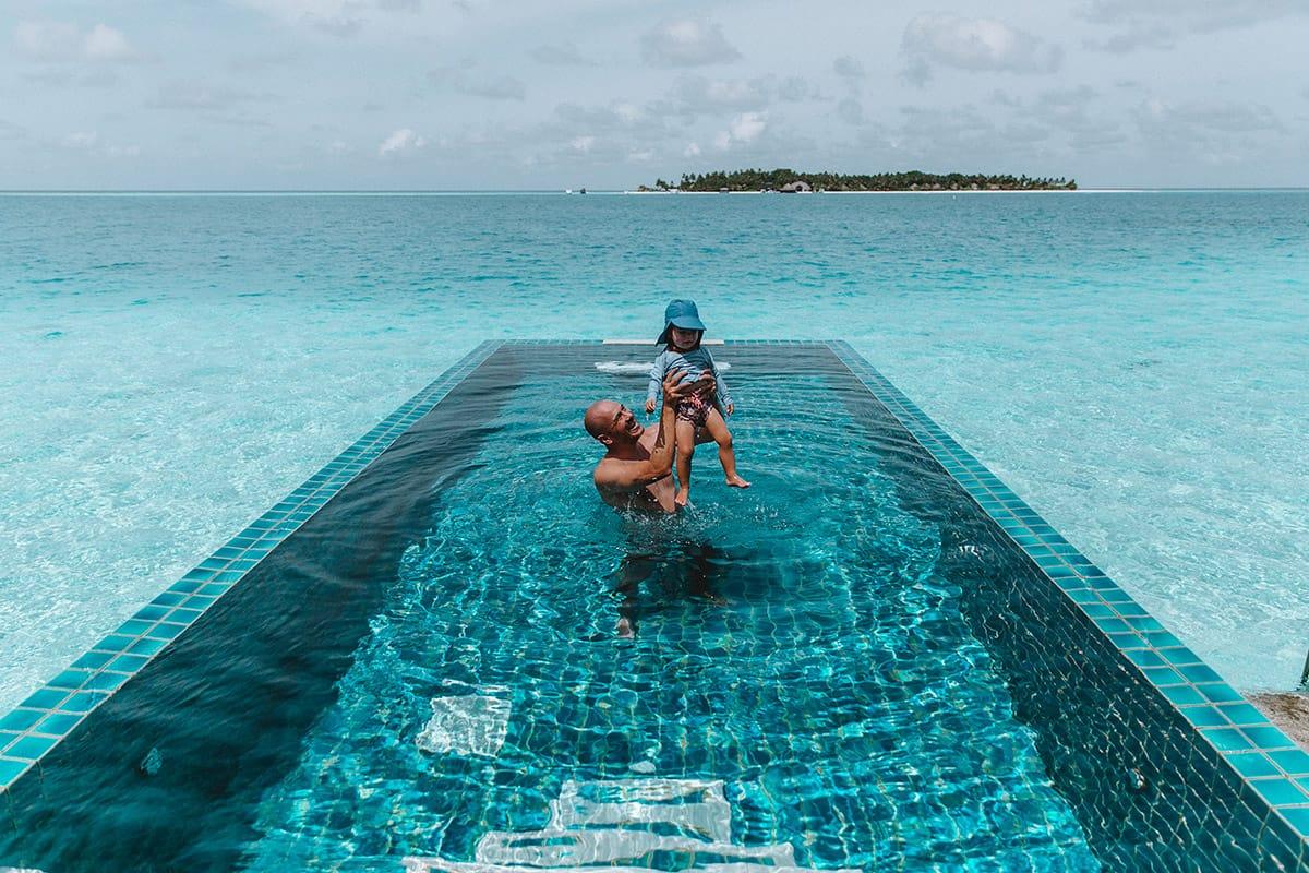 Dad playfully holding child in crystal-clear pool at Angsana Velavaru Maldives.