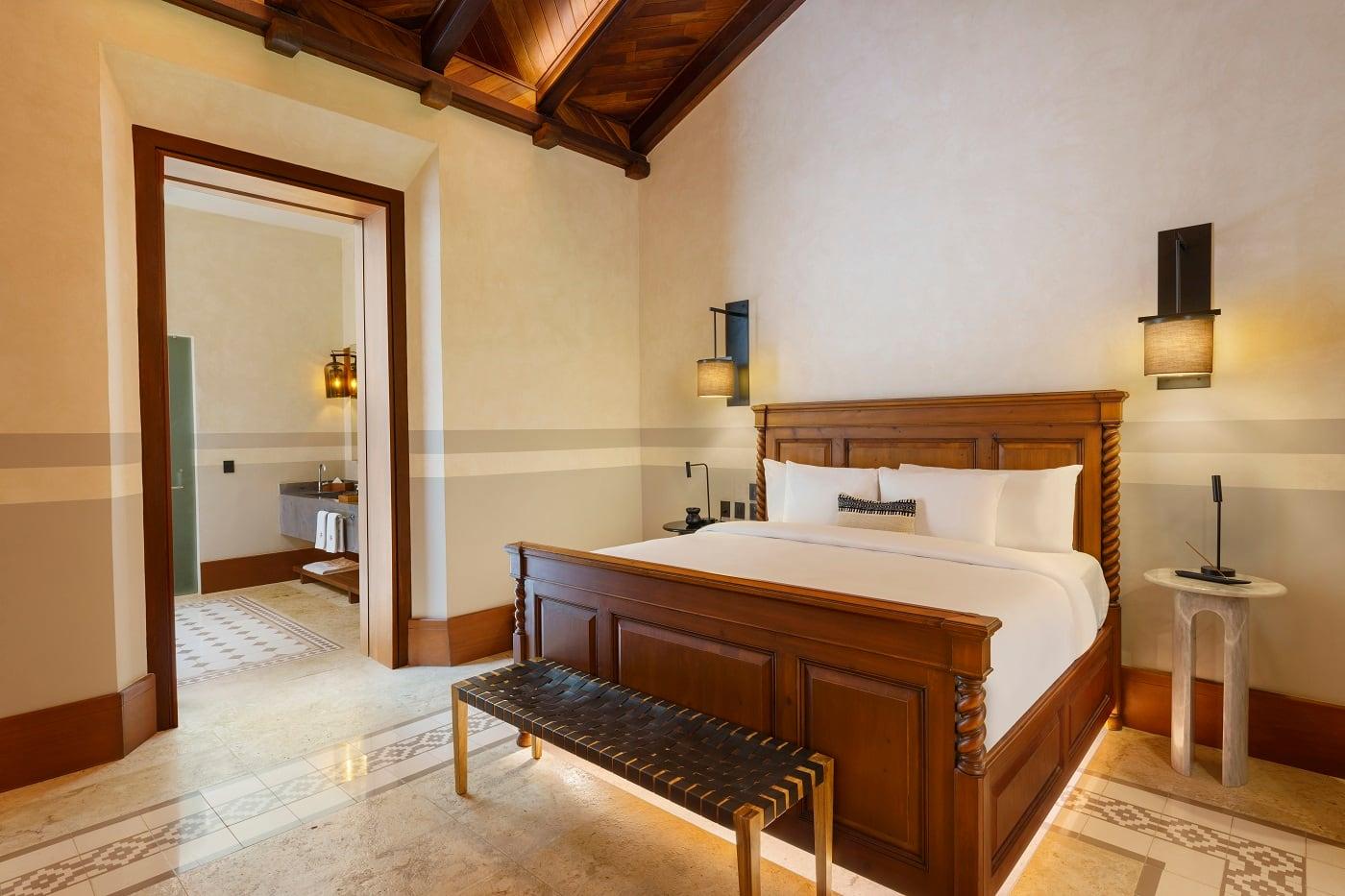 Wooden bed with white linens, beside lit lamps in Hacienda Xcanatun, Angsana Heritage Collection suite.
