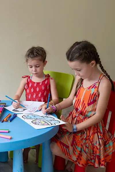 Two children enjoying creative coloring activities at the Angsana Velavaru Kids Club, a vibrant space for fun and exploration in the idyllic Maldives.
