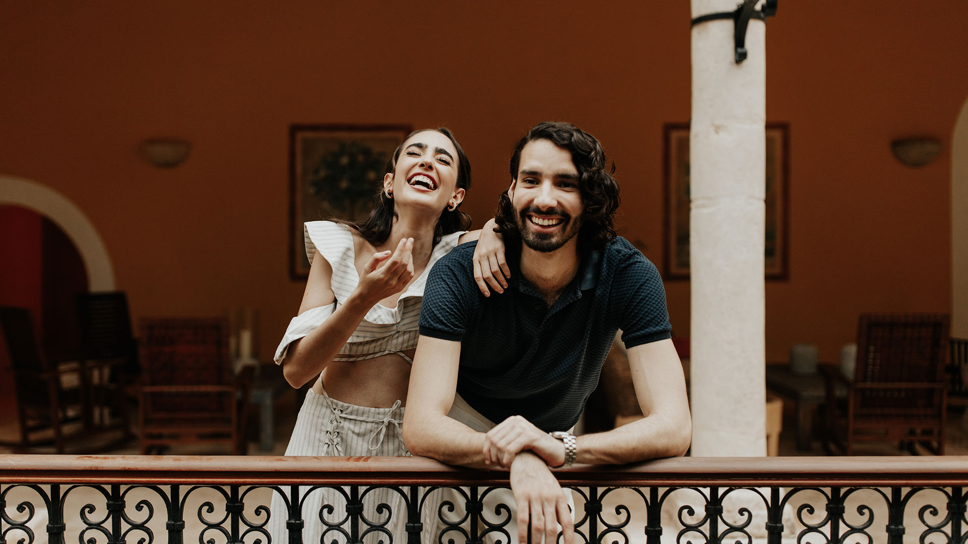 Smiling couple leans on ornate railing at Hacienda Xcanatun, Angsana Heritage Collection, indoors.
