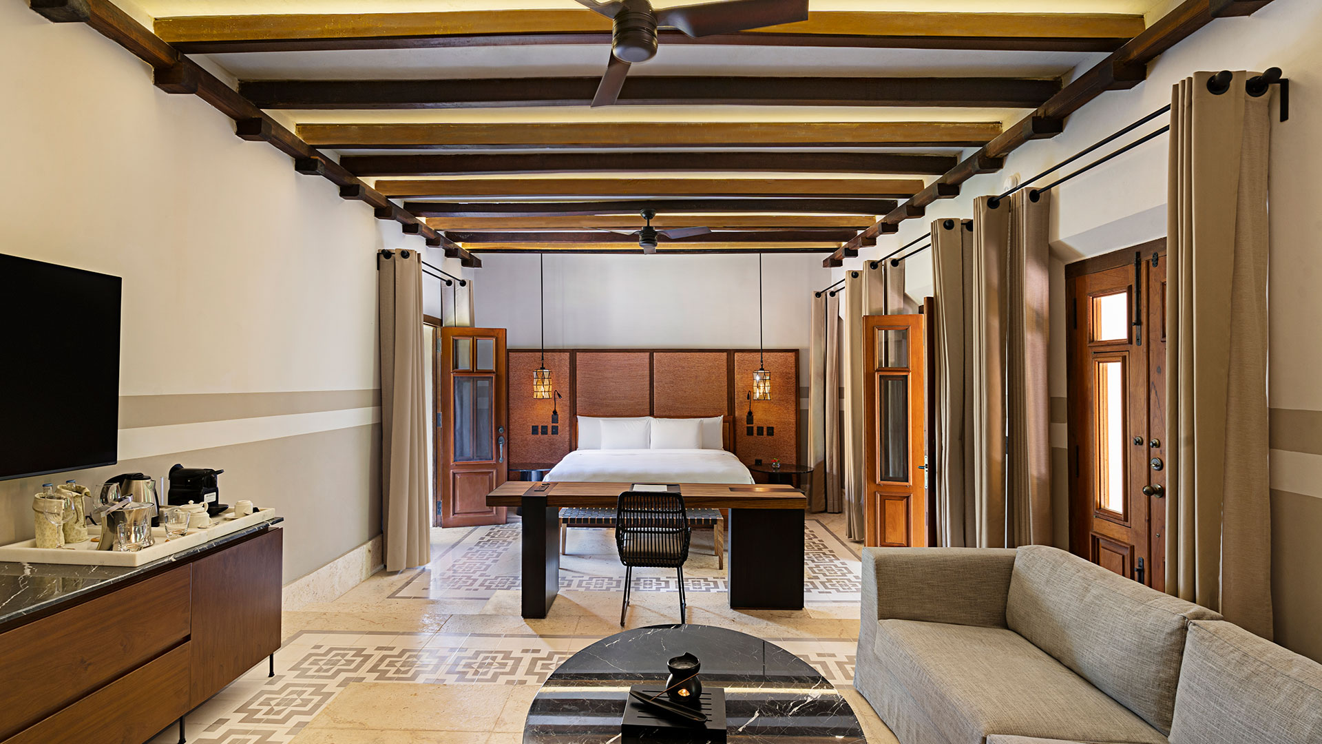 Bed positioned in elegant room with wooden beams, cozy sofa, and stylish decor at Hacienda Xcanatun, Angsana Heritage Collection.