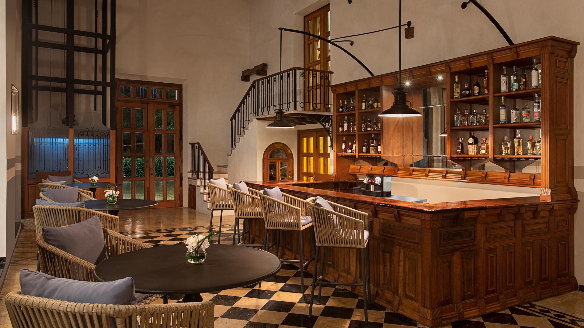 Elegant bar with wooden shelves and rattan chairs, illuminated warmly, in Hacienda Xcanatun, Angsana Heritage Collection.
