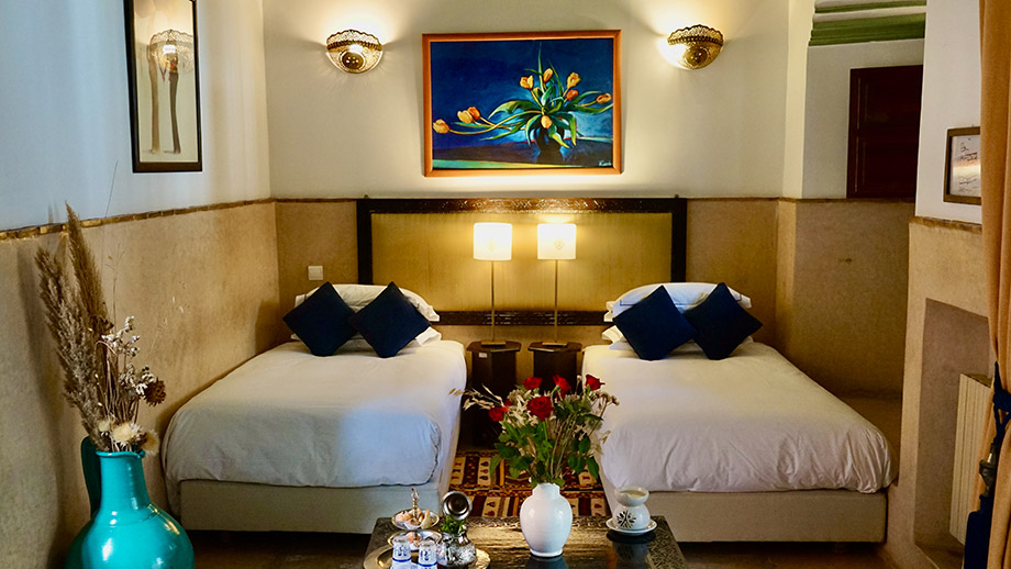 Twin beds with blue pillows beneath colorful art, flanked by lamps, in Angsana Riads Collection - Marrakech, Si Said Deluxe Twin.