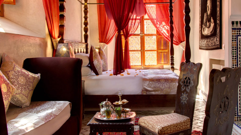 Elegant room features a bed with red drapes, Moroccan decor, and tea set; Angsana Riads Collection - Marrakech, Si Said Ambassador Suite.