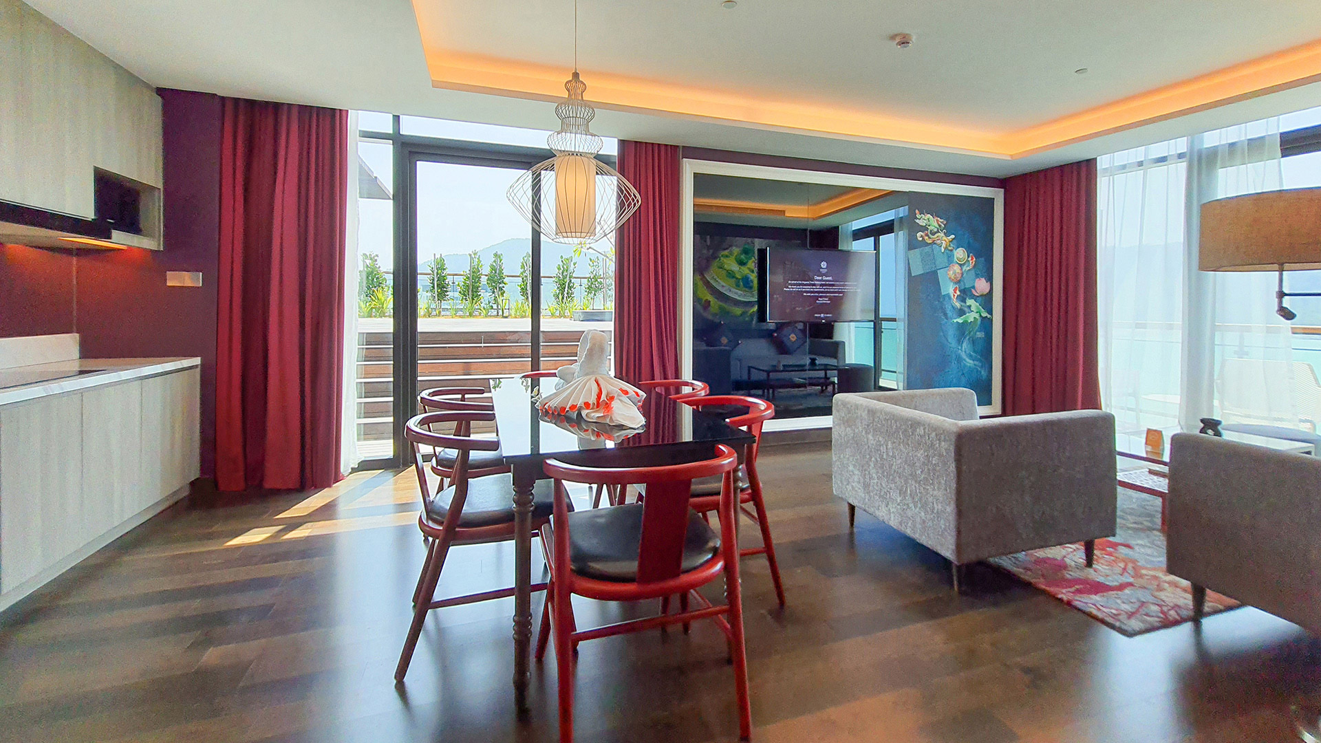Dining table set with red chairs faces TV in Angsana Teluk Bahang Penang suite's bright living area.