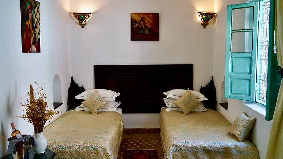 Cozy twin beds adorned with pillows, vibrant paintings on walls, at Angsana Riads Collection - Marrakech Blanc Studio Twin.