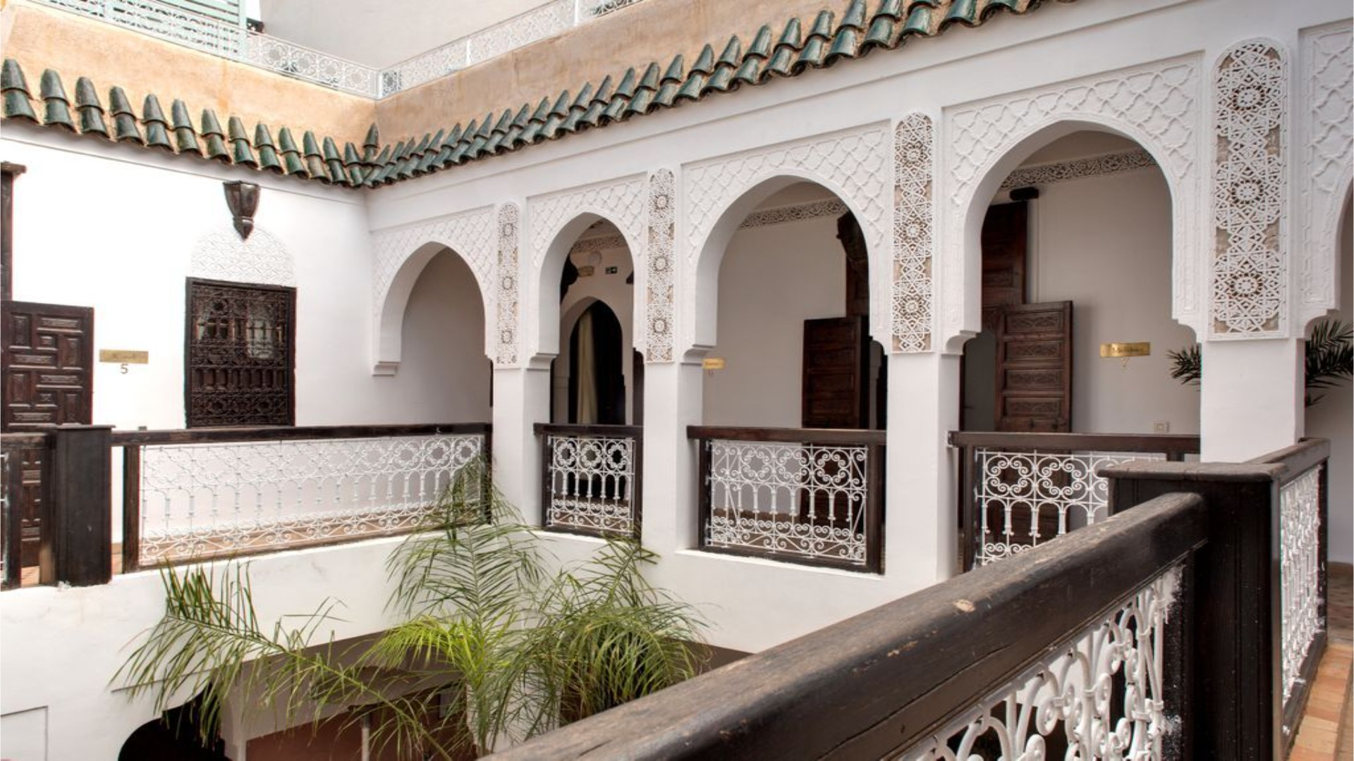 Arched white balcony surrounds courtyard with ornate railings at Angsana Riads Collection - Marrakech, Riad Blanc.