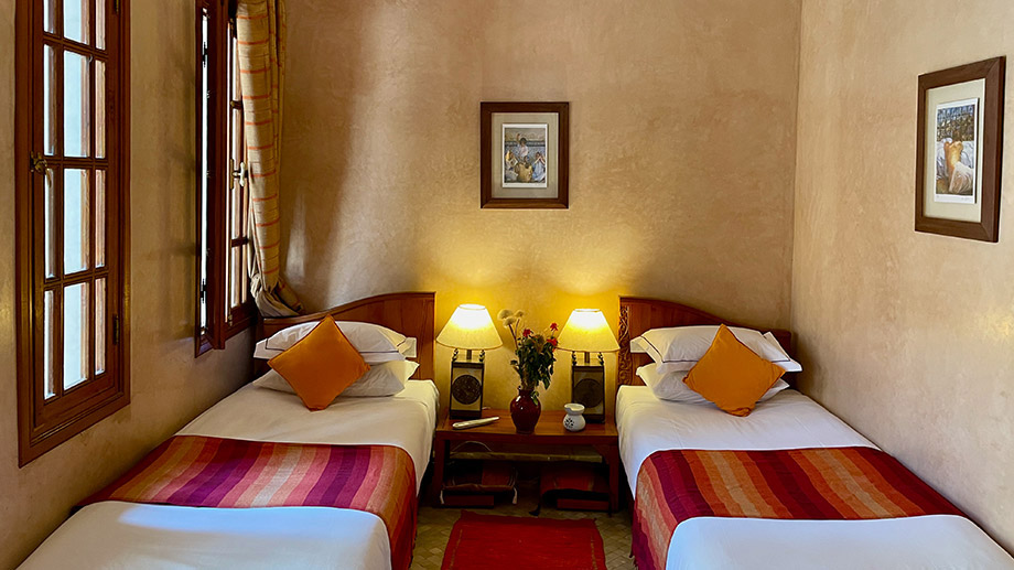 Twin beds with colorful blankets, lamps glowing on a wooden nightstand, framed art; Angsana Riads Collection - Marrakech, Lydines Studio Twin.