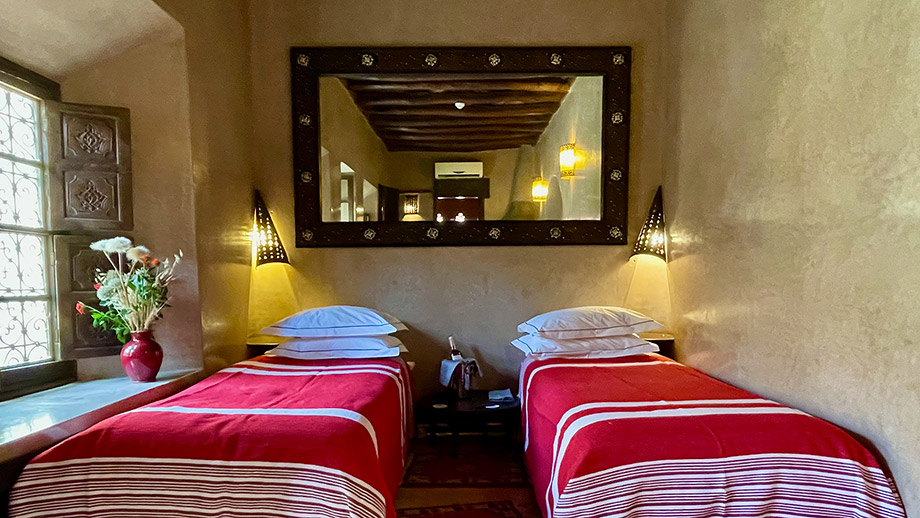 Twin beds with red covers rest under a large mirror in a cozy Angsana Riads Collection room, Tiwaline Deluxe Twin.