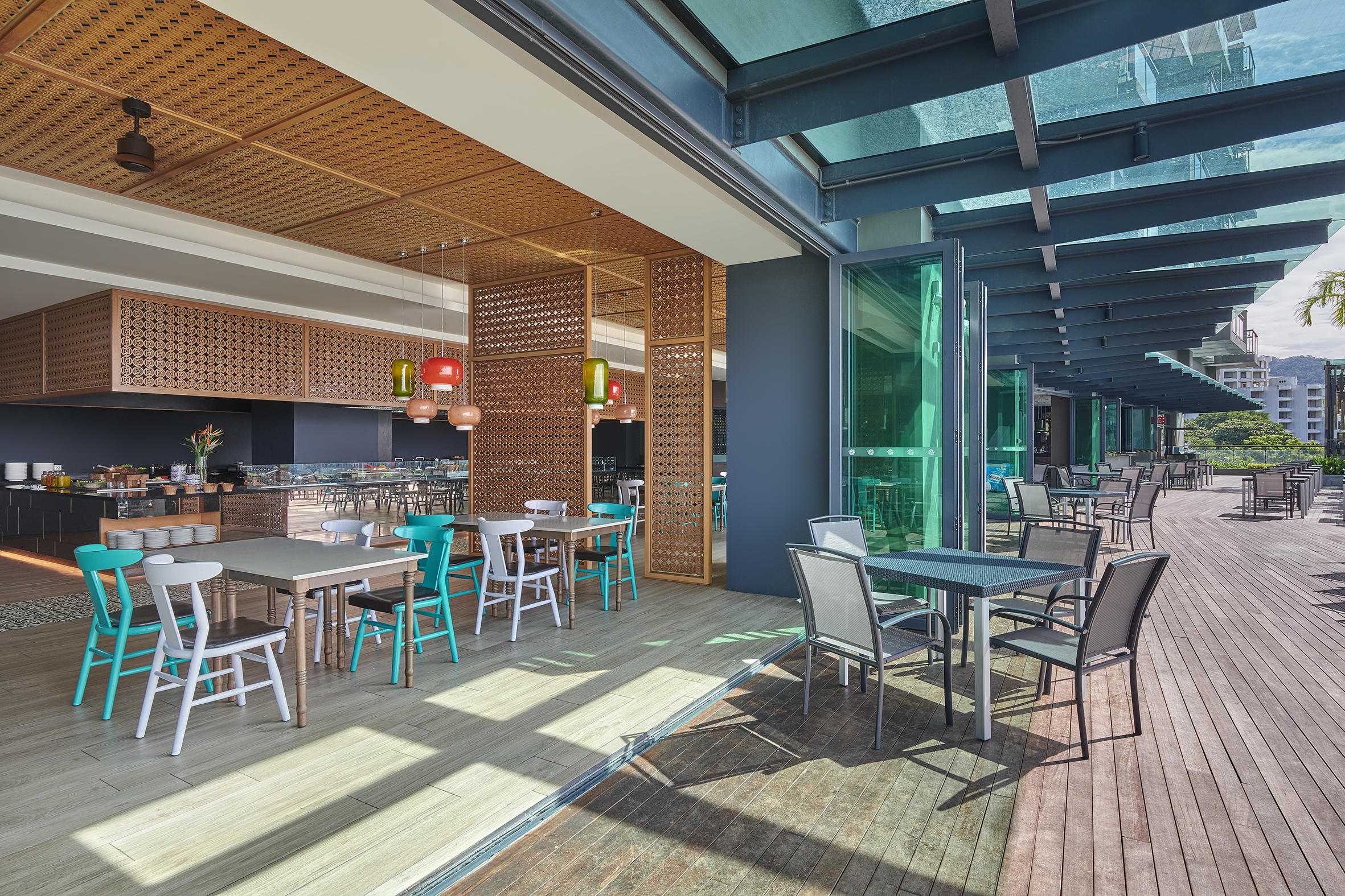 Dining tables under colorful lights open to a sunny deck at Angsana Teluk Bahang Penang.