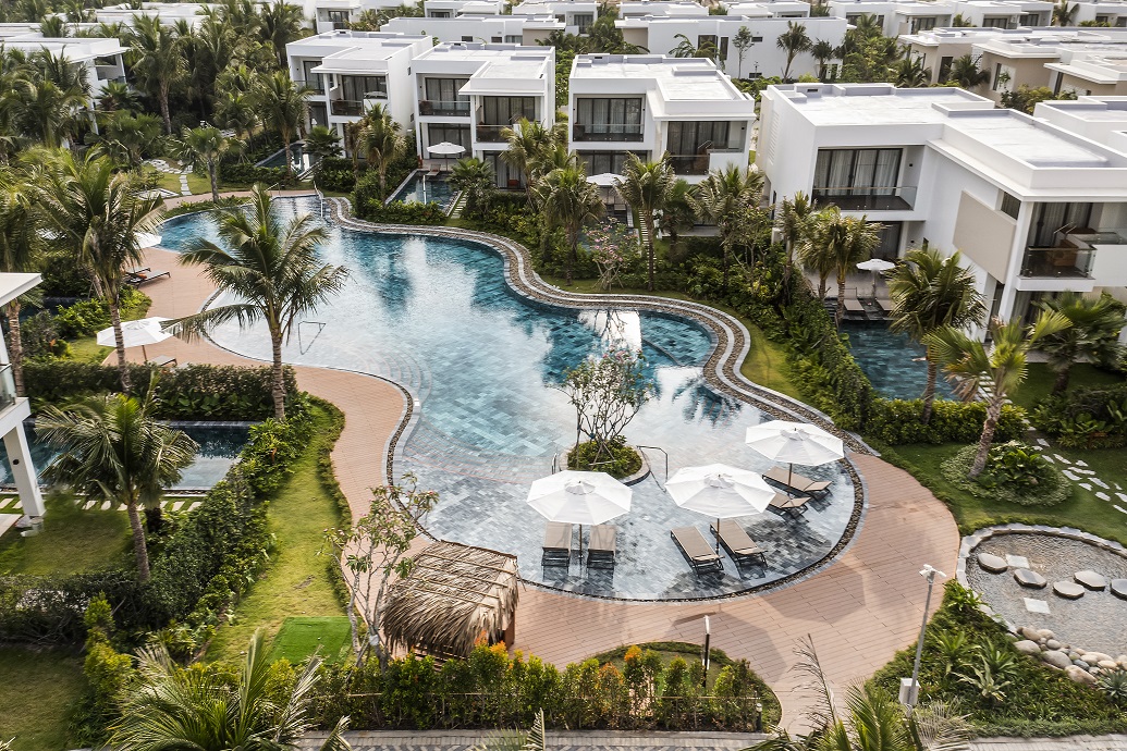 Winding pool amidst villas and palms at Angsana Ho Tram Vietnam, surrounded by lush greenery.