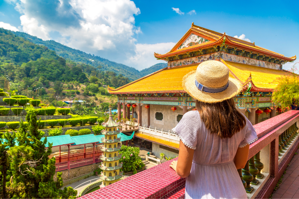 Woman in straw hat admires temple view with mountains at Angsana Teluk Bahang Penang.