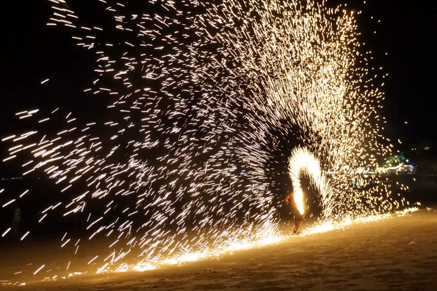 Fire performer creates spark shower on beach at Angsana Teluk Bahang Penang, dazzling night display.